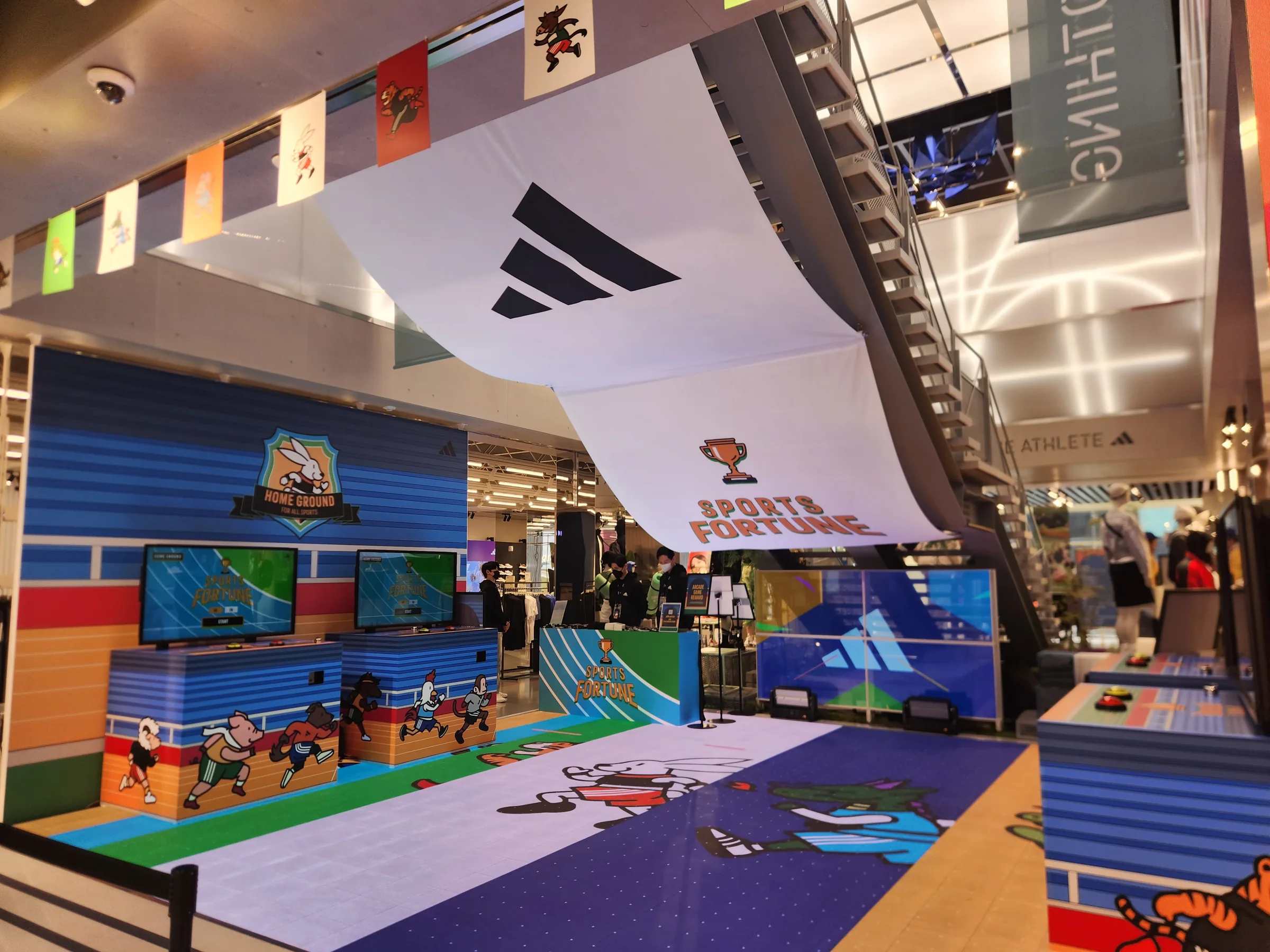 Two machines along the left graphic wall beneath an adidas banner, with character imagery on the LED floor