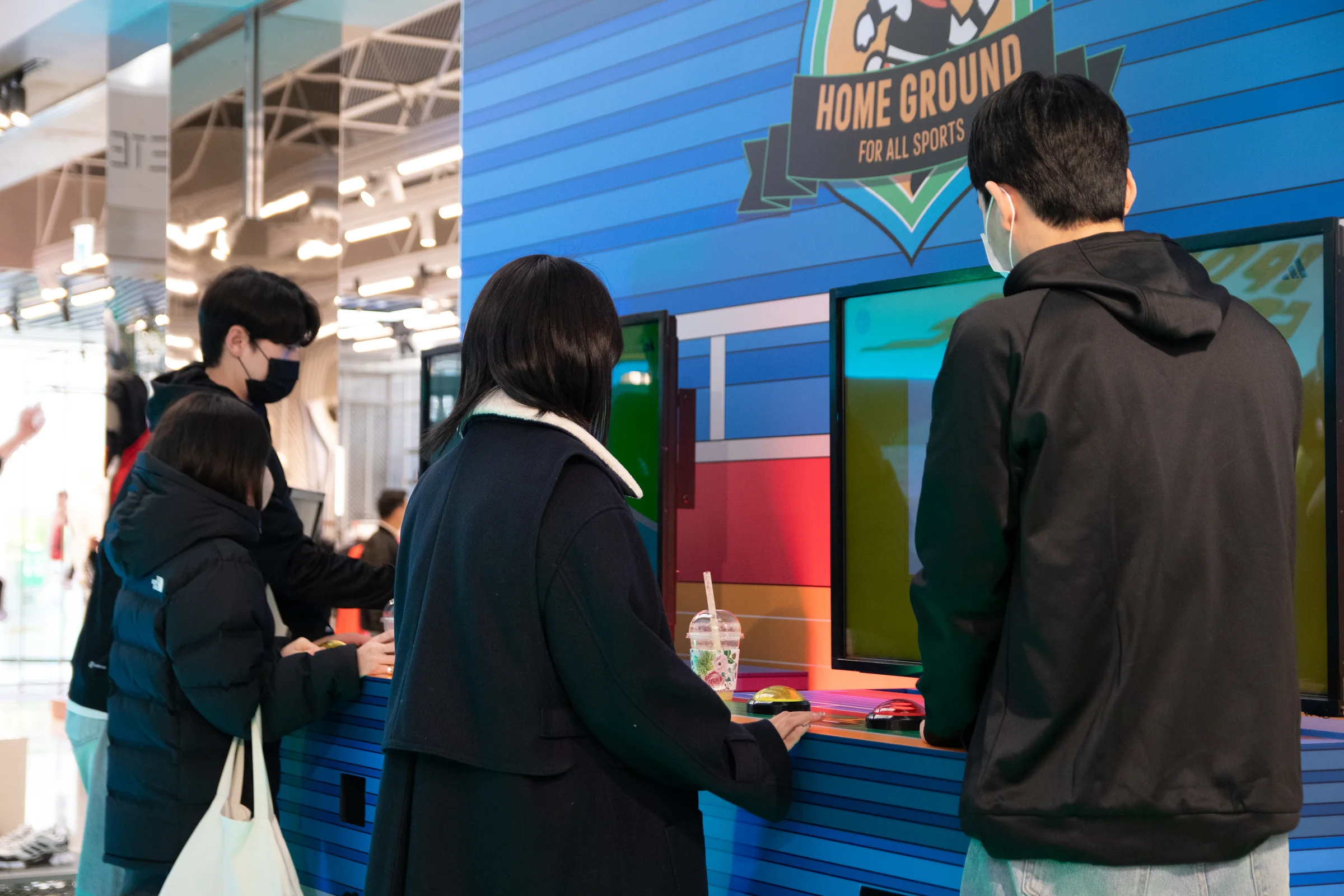 Two participants look at a machine screen together under the HOME GROUND badge.