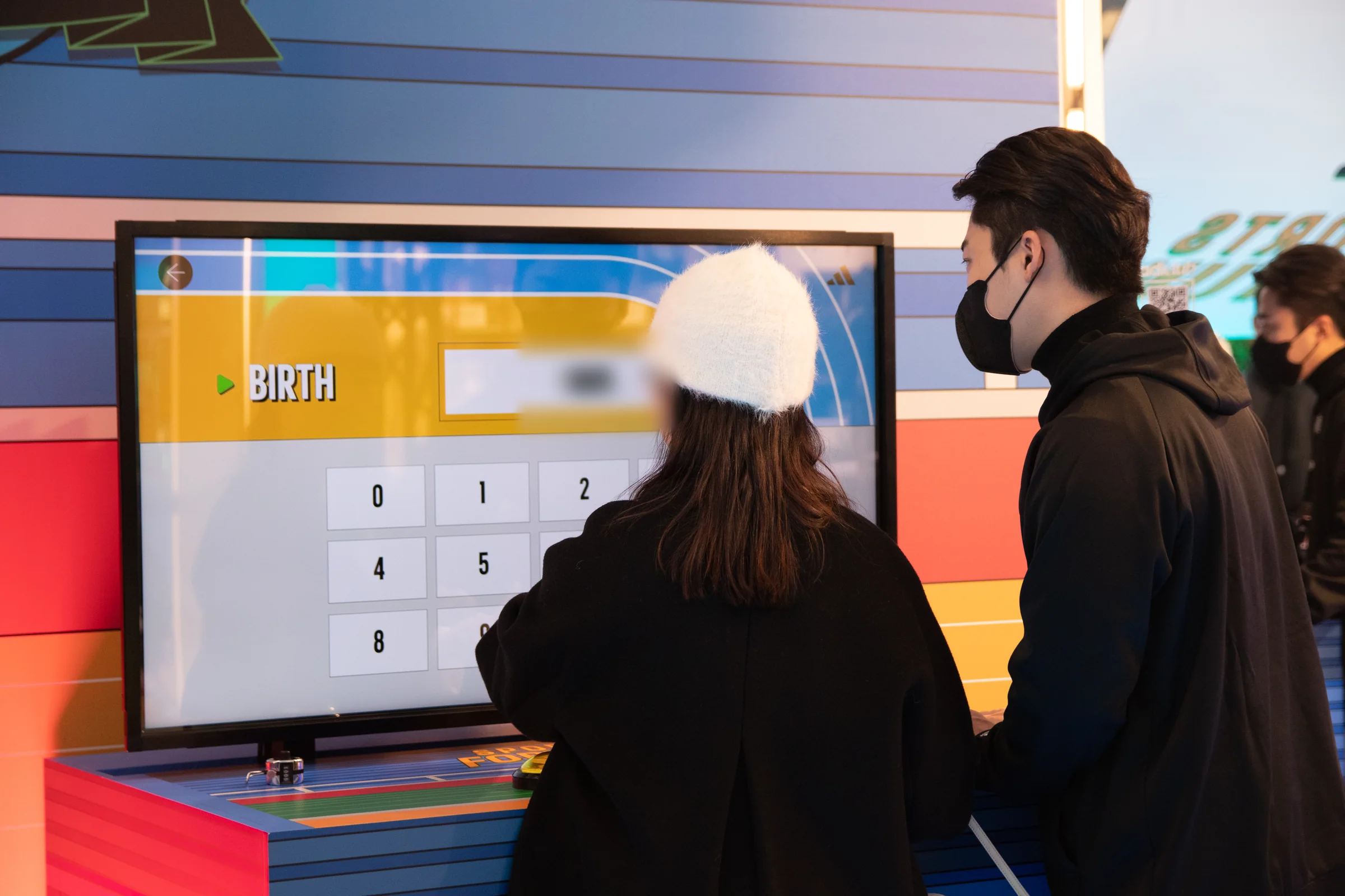 A participant enters their birth date at a machine as another person watches.