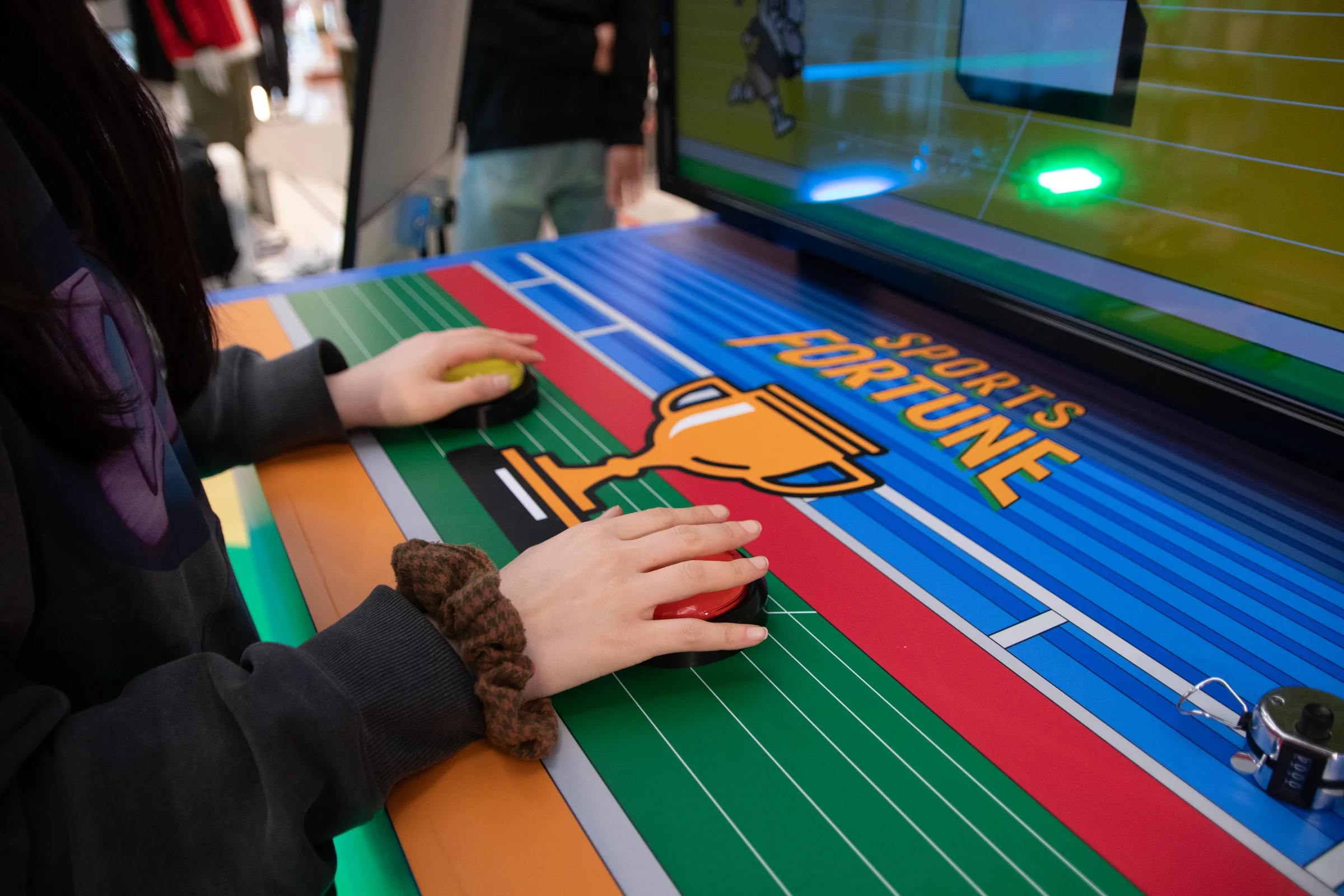 A participant presses yellow and red buttons on a trophy-patterned console.