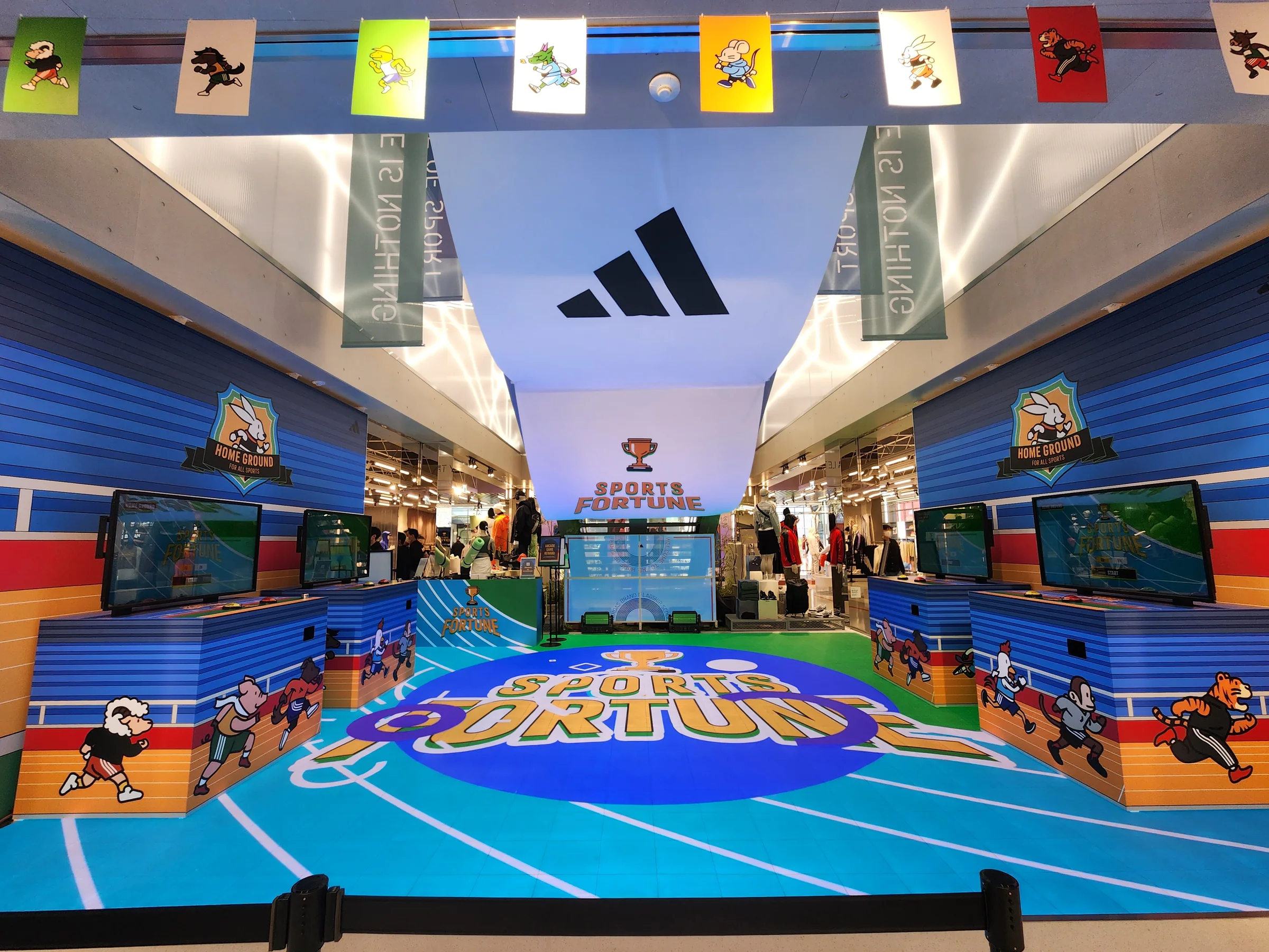 Front view of the game zone, with machines on either side, a SPORTS FORTUNE scene on the LED floor and store displays beyond