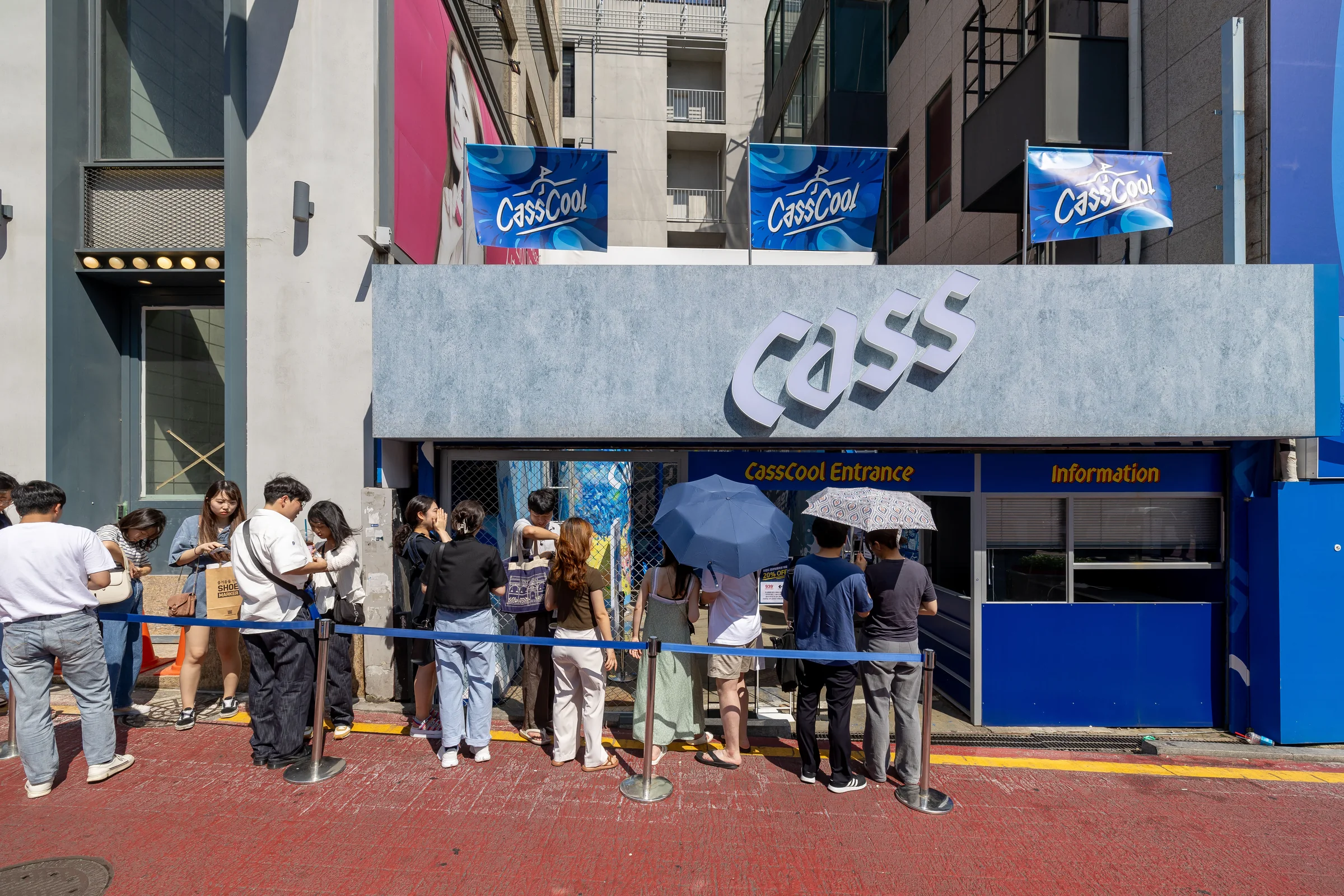 CASS 간판이 달린 메인 팝업 입구 앞에 양산을 쓴 관람객들이 줄을 서 있다.