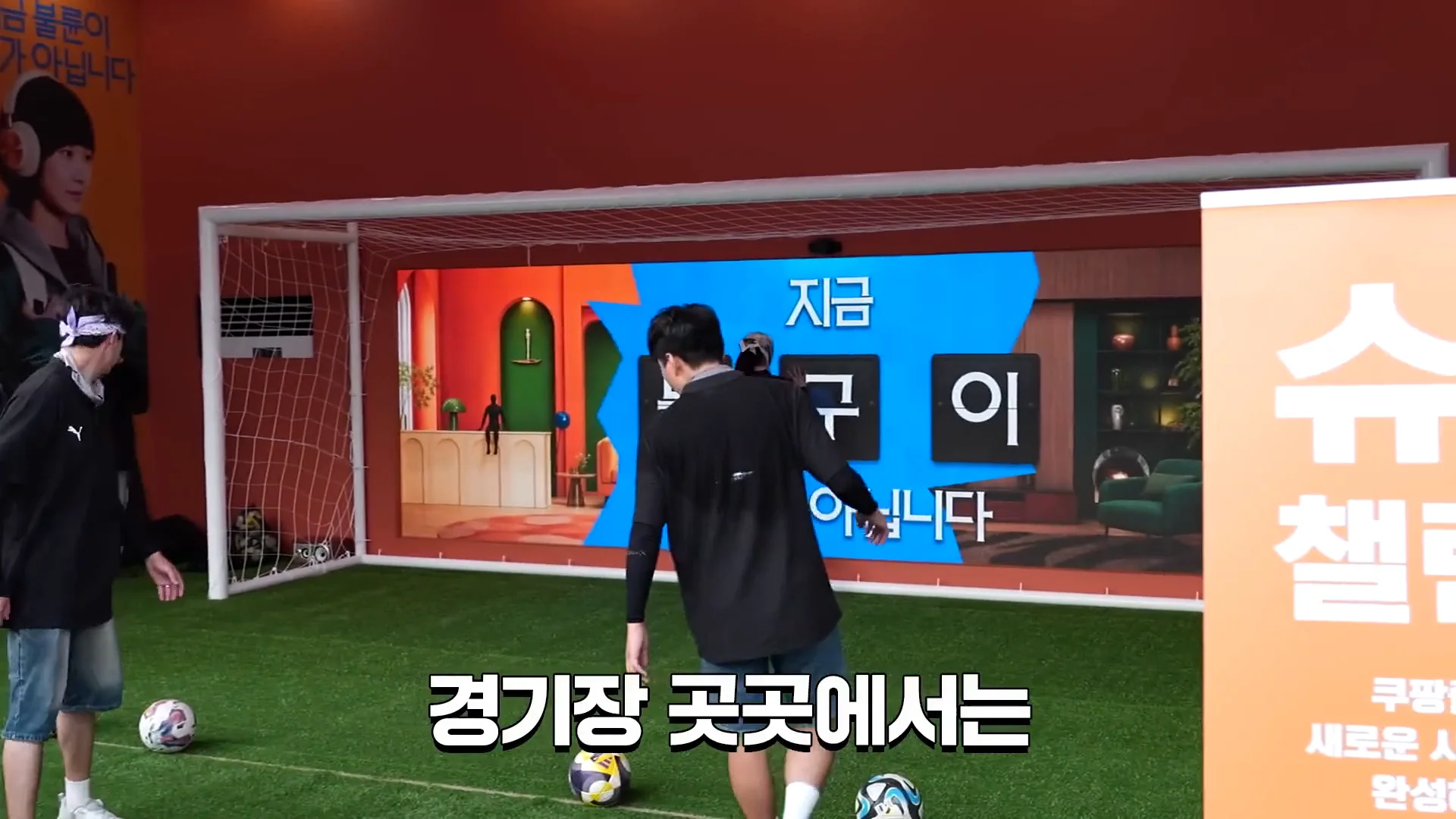 검은 옷의 참가자가 LED 골대를 향해 공을 차고 있다.