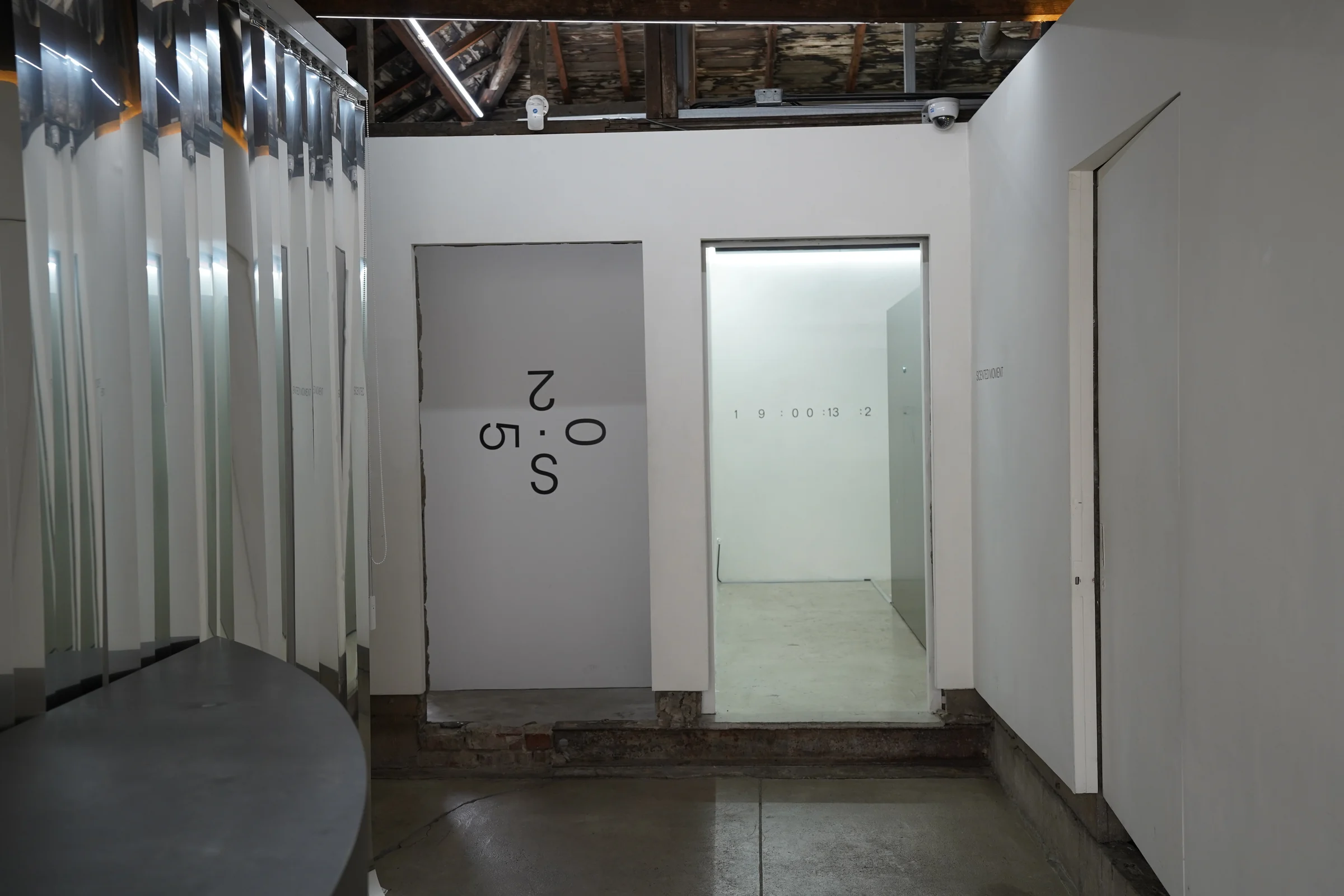 Two adjacent doorways on the third-floor corridor: the 025S photo booth exterior is visible through the left, and the white cube room through the right.