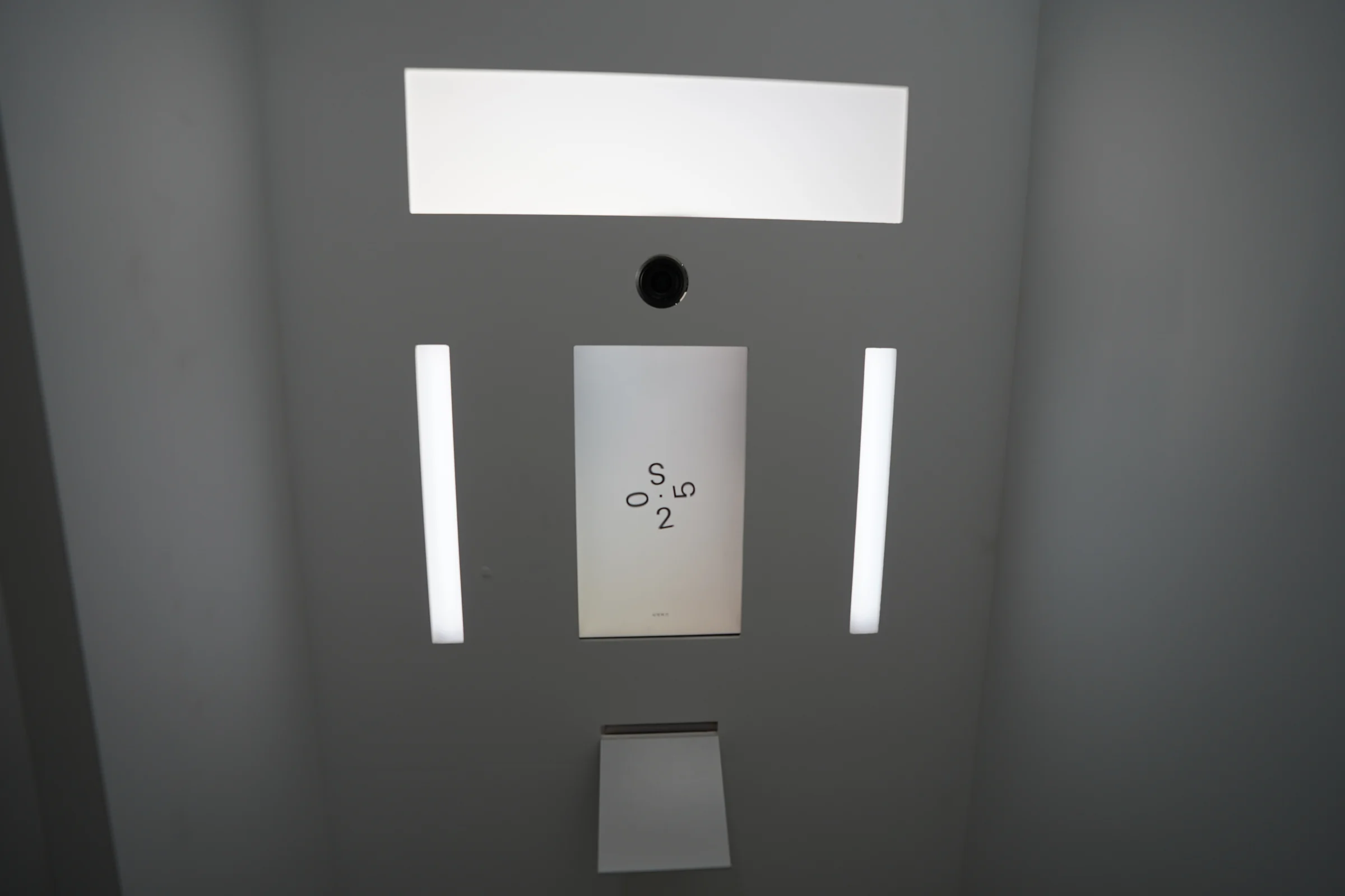 The front of the white booth, with an overhead light panel, camera opening, portrait screen, side light bars and lower collection tray.
