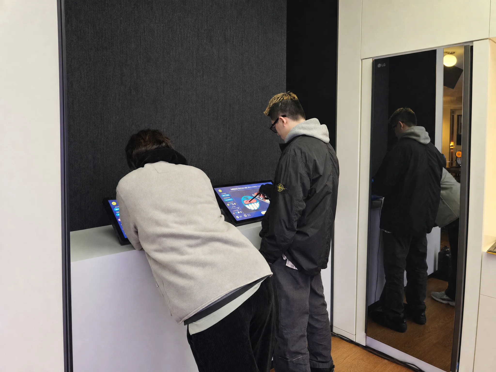 白いカウンターの2台のタブレットで絵を描く二人。