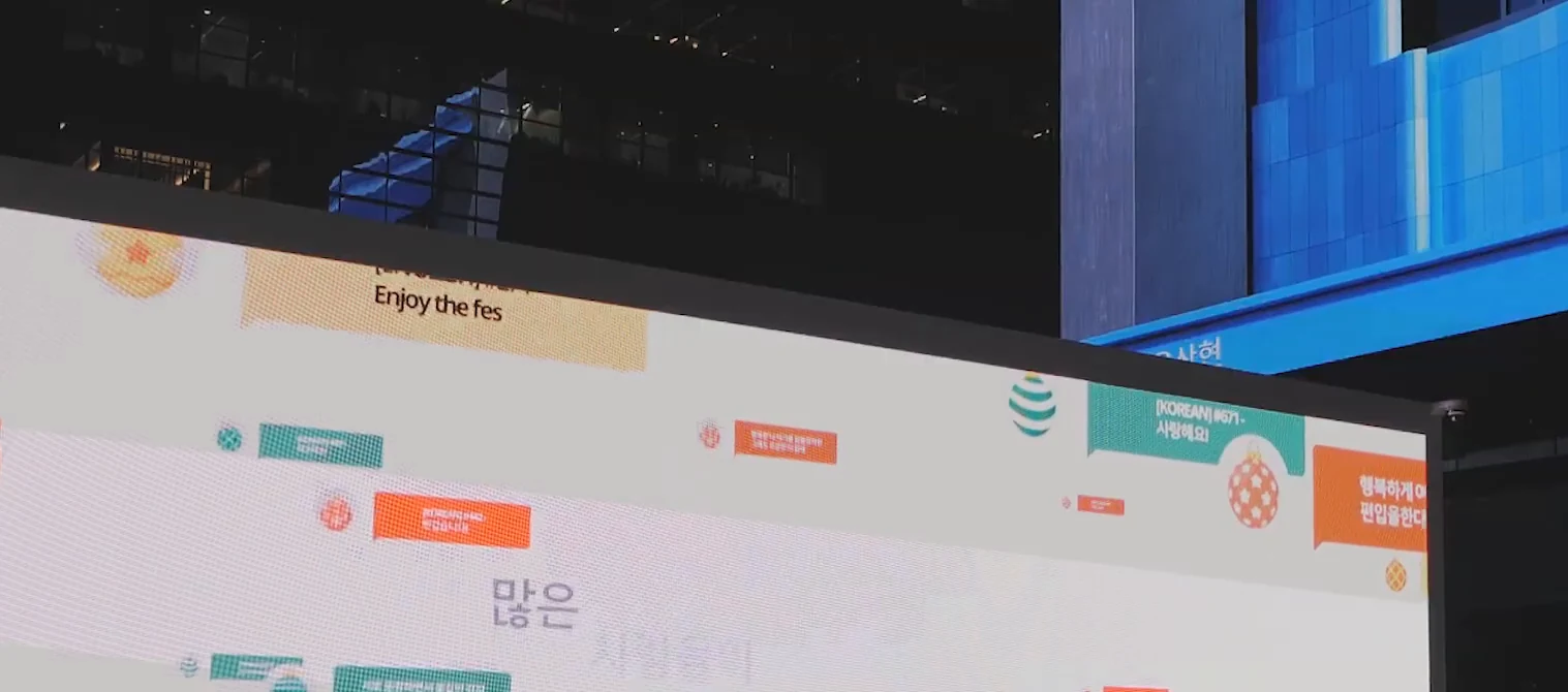 흰 LED 월에 색색의 메시지 카드가 떠 있고 위로 빌딩 전광판이 보인다.