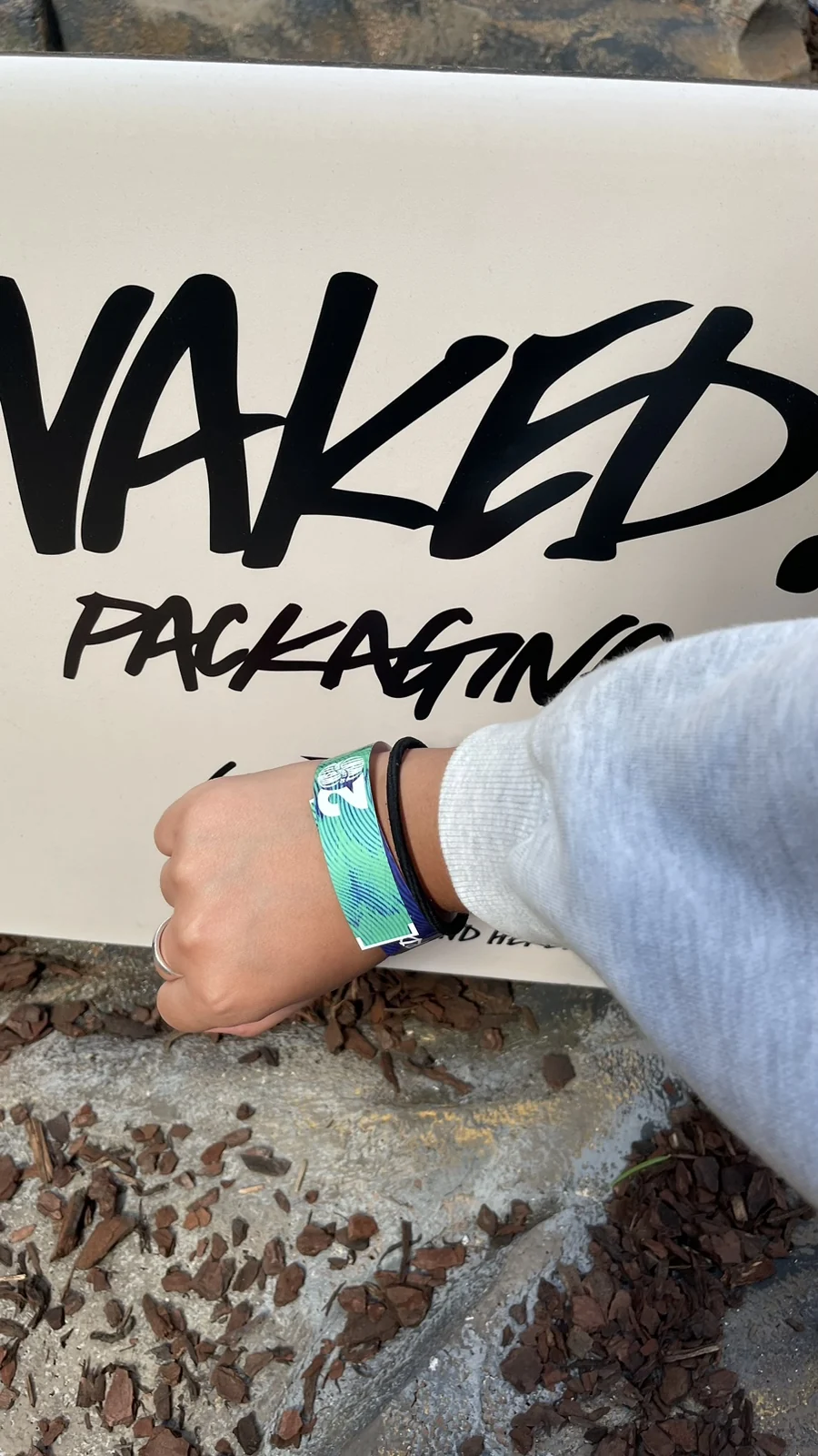NAKED PACKAGING 팻말에 팔찌를 댄 손목