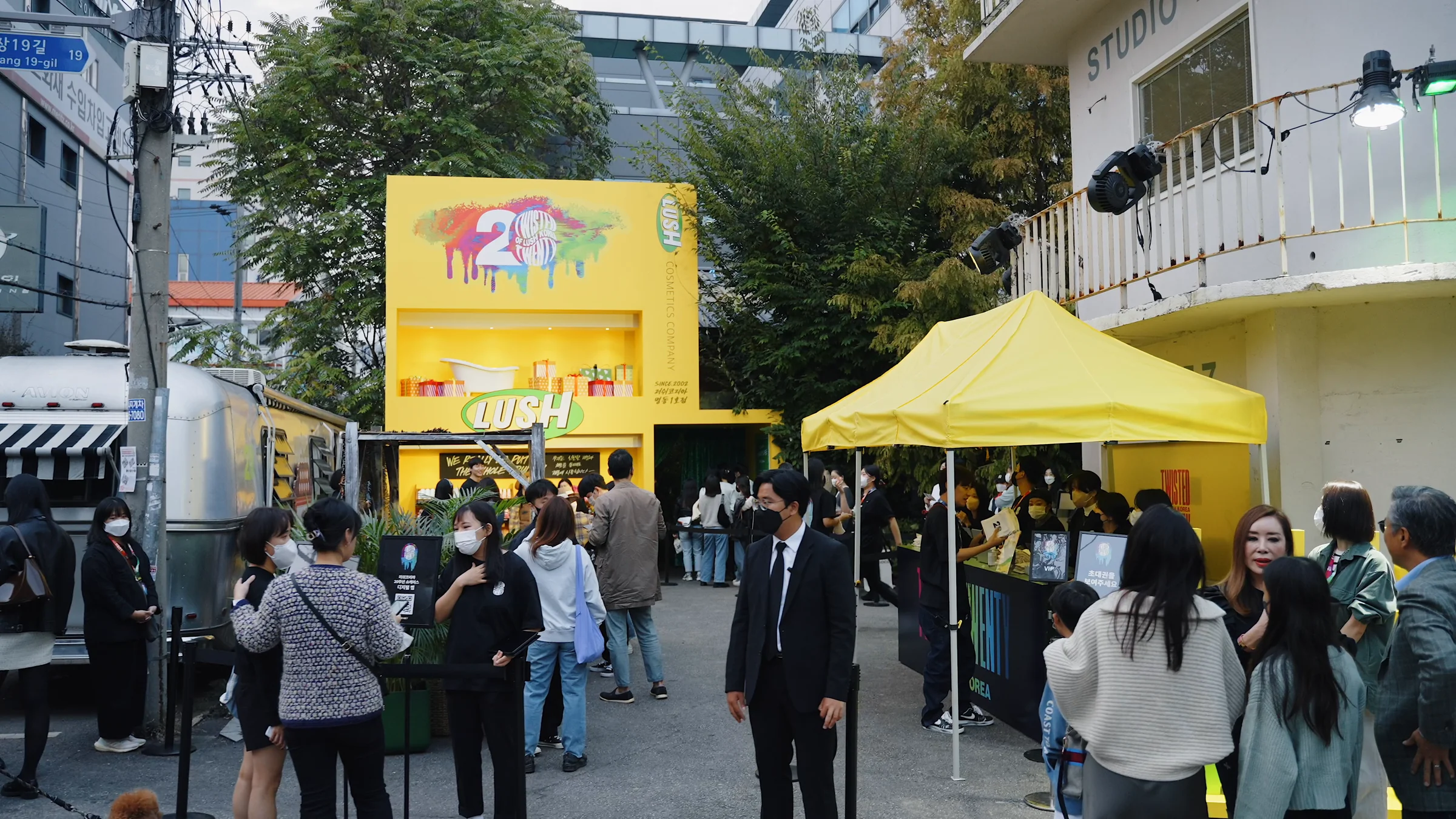 노란 러쉬 마켓 부스와 천막 앞 입구 마당에 모인 방문객들