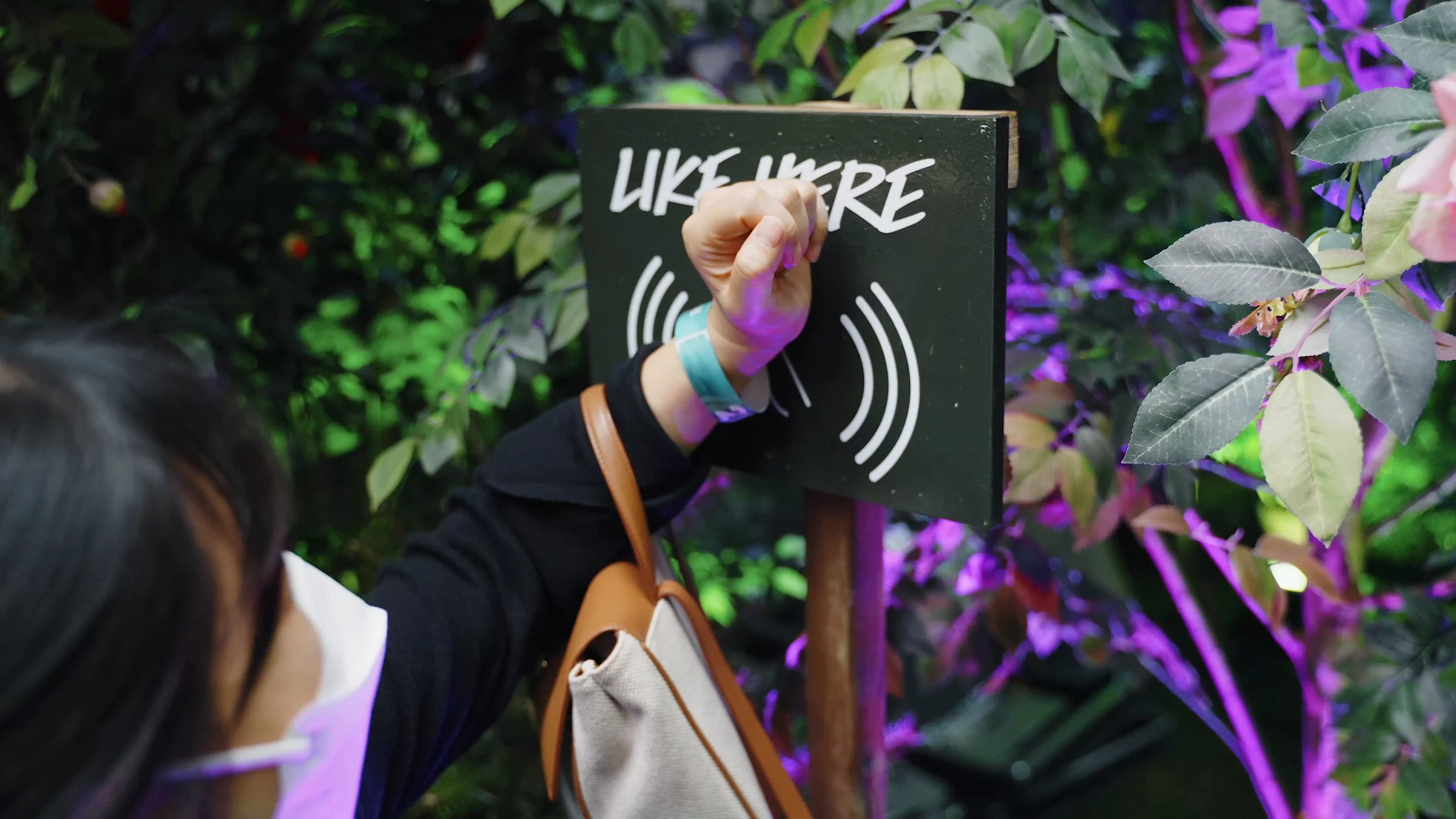 정원의 LIKE HERE 표식에 RFID 팔찌를 댄 손목을 갖다 대는 방문객