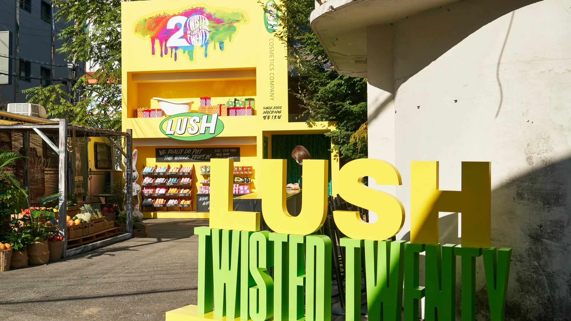 입구의 초록 LUSH TWISTED TWENTY 사인과 노란 러쉬 마켓 부스
