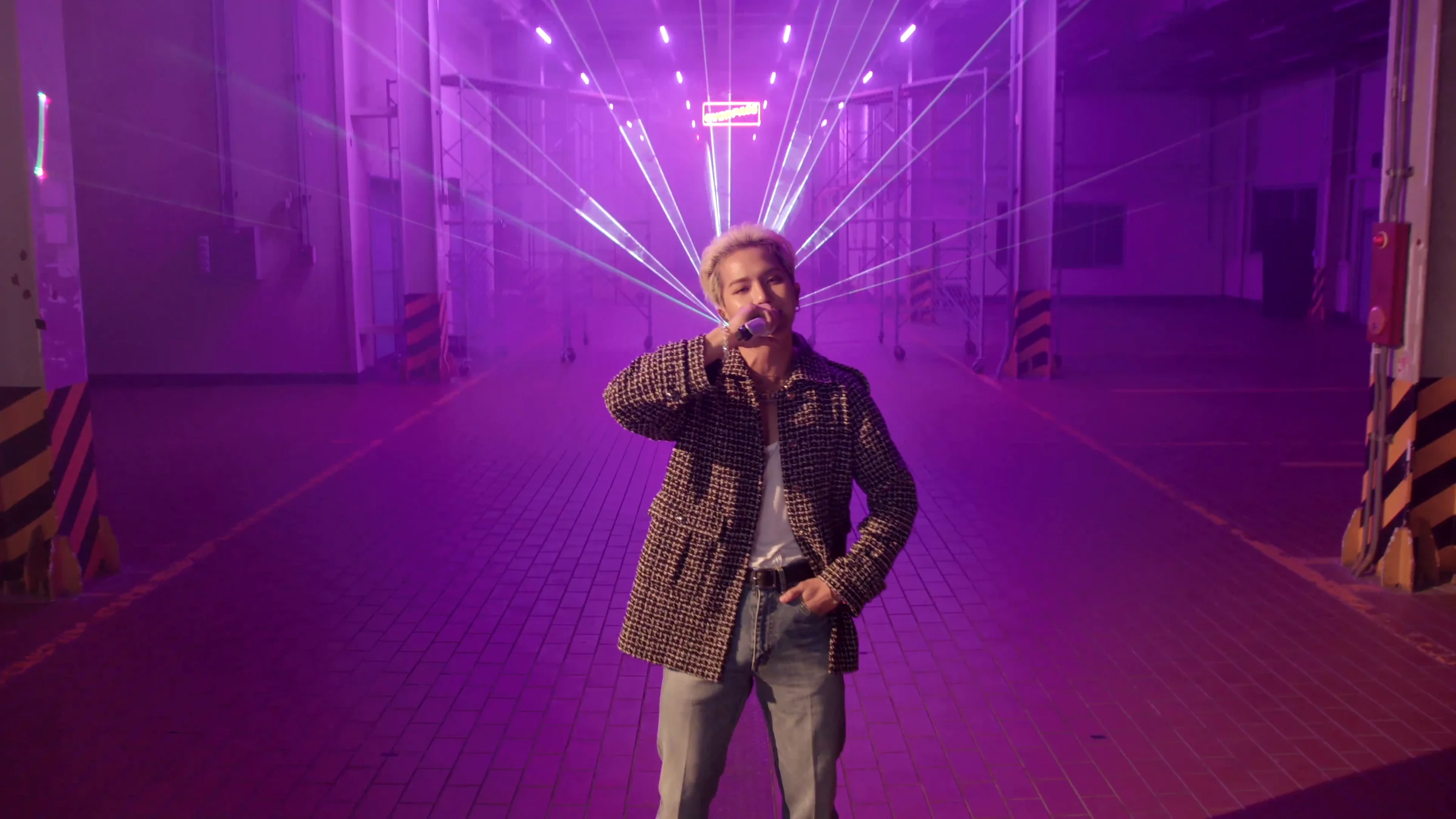 MINO standing before a violet fan of beams at the far end of the warehouse