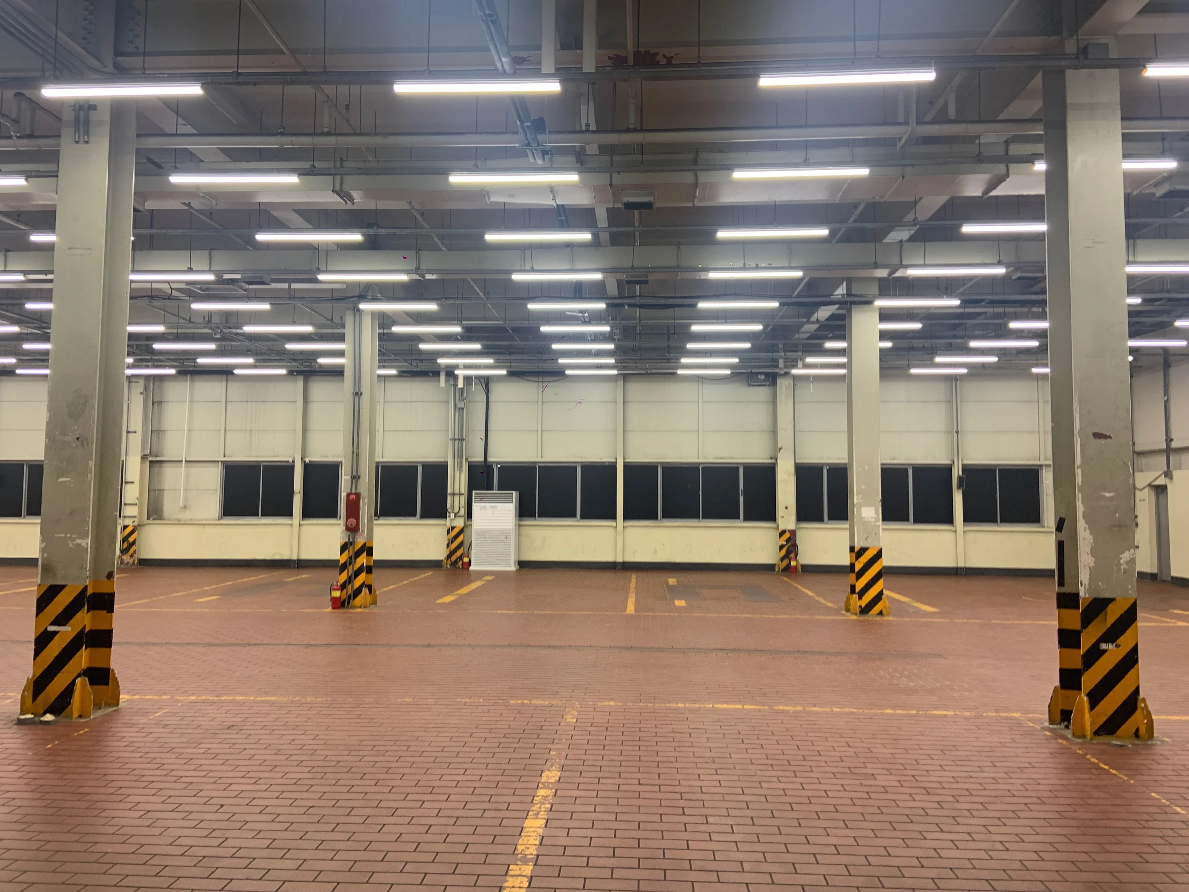 An empty warehouse under fluorescent lights, with columns and yellow floor markings