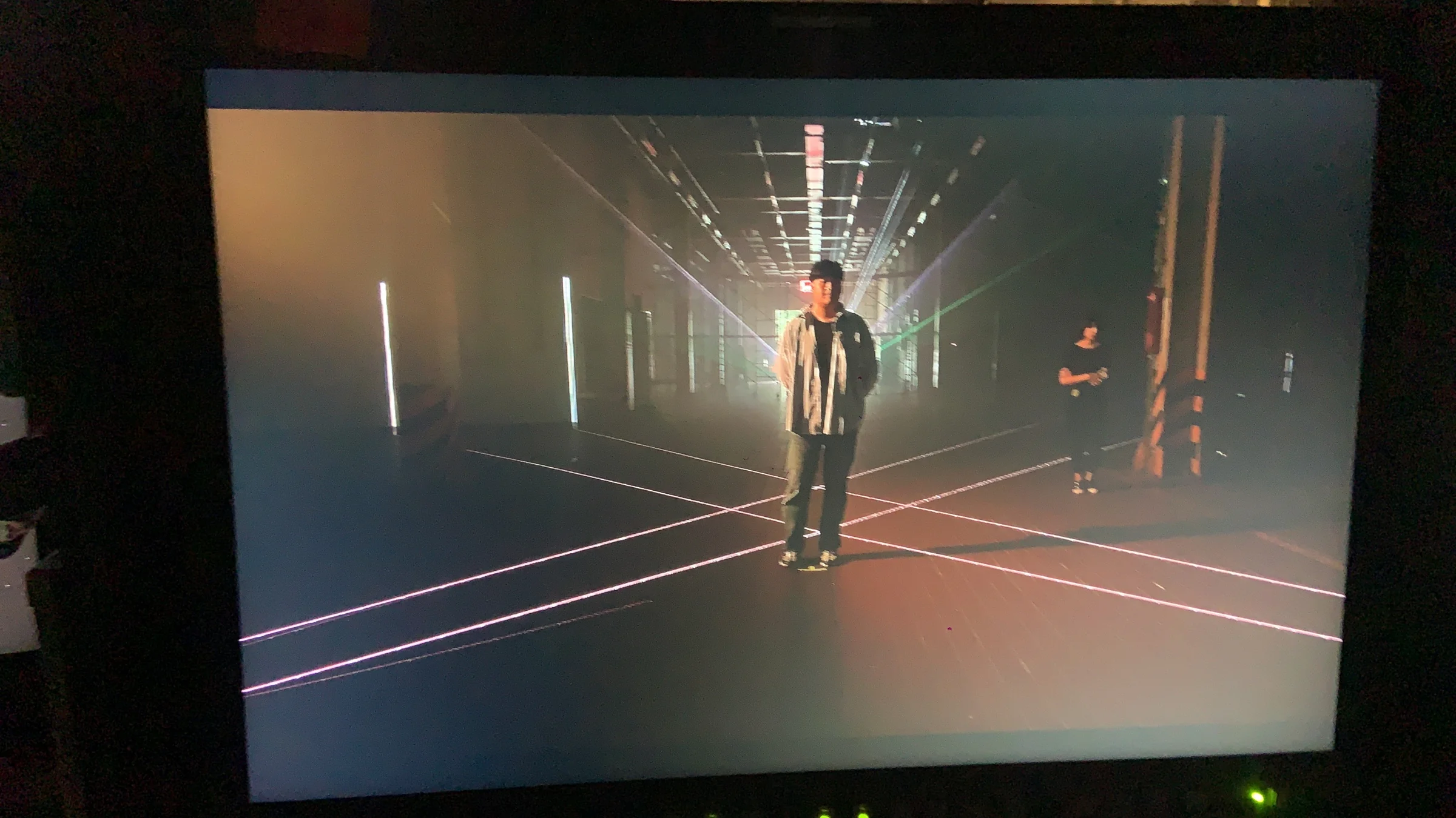 A filming monitor showing a performer and laser beams across the warehouse