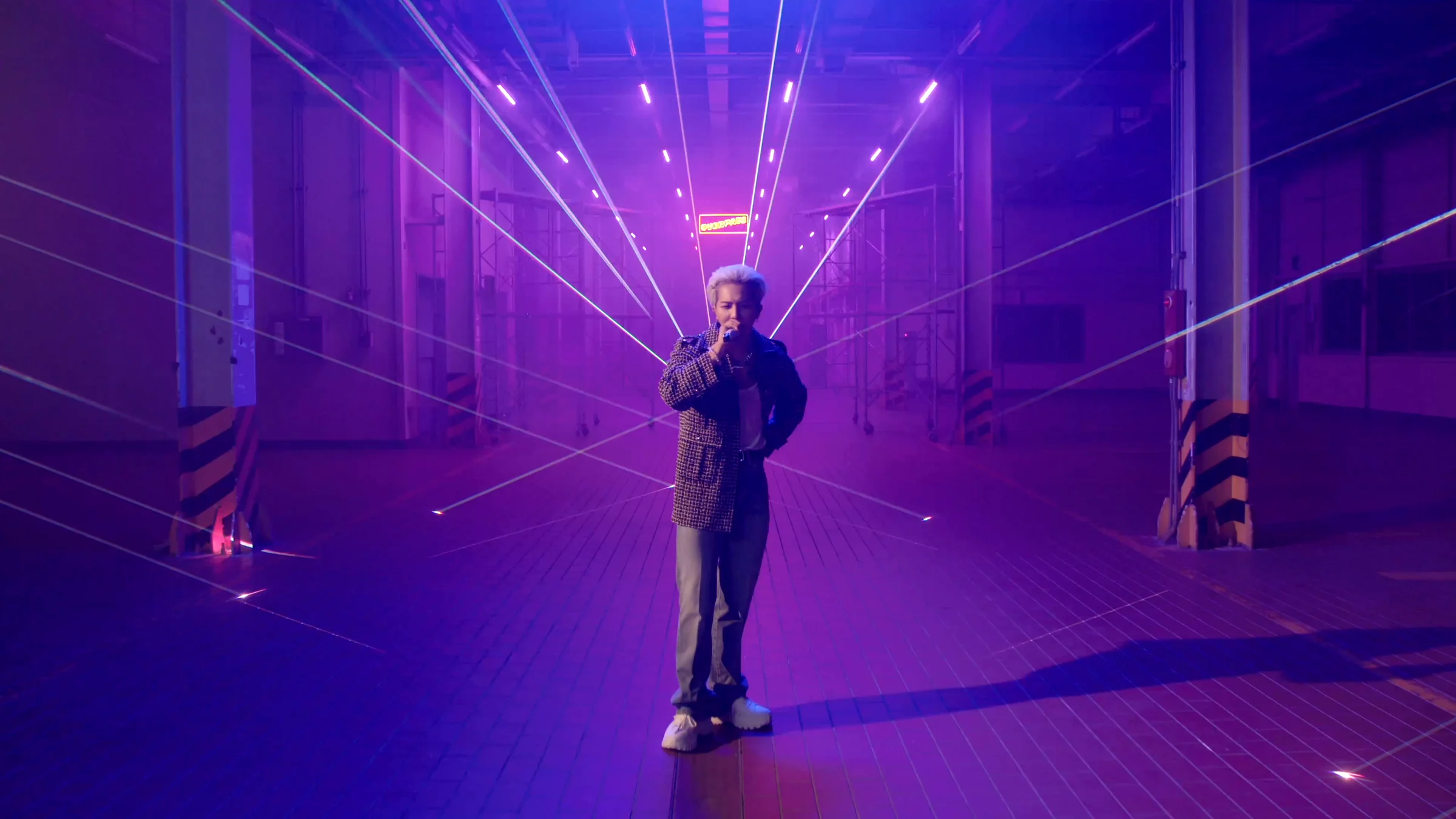 MINO standing before violet fan-shaped beams spreading from the far end of the same warehouse