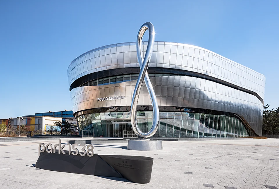 The silver curved facade of POSCO Park1538 Exhibition Hall and a sculpture in its forecourt