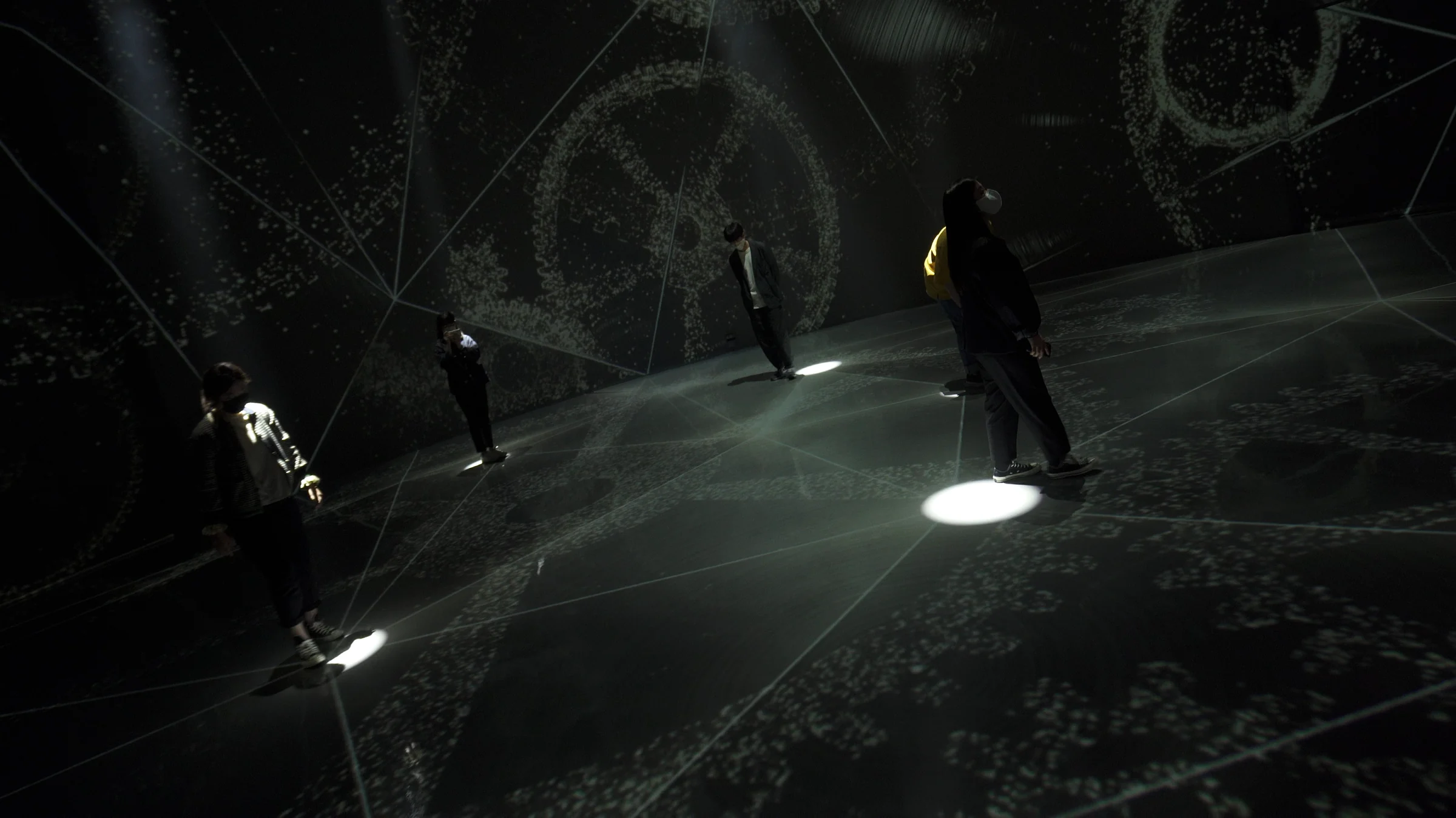 A circular hall filled with wireframe gears. Each visitor has a white circle of light beneath their feet.