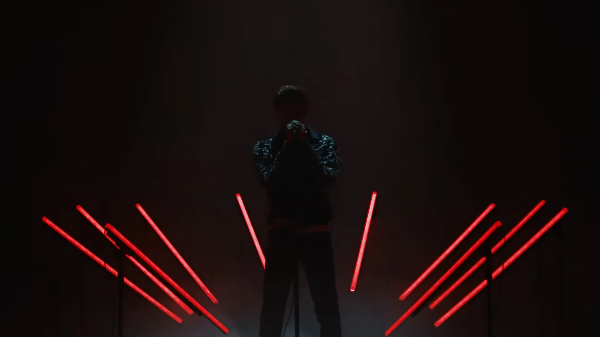 Red bars illuminate either side of the performer in darkness