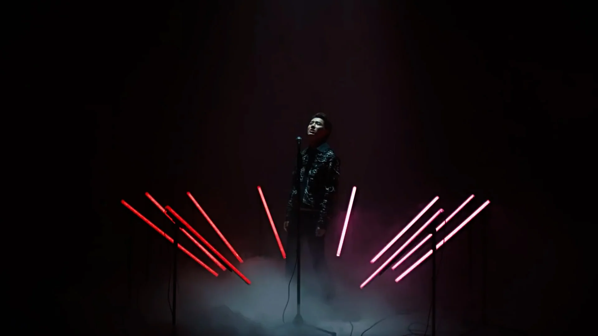 Red light bars fan out on either side of the performer in darkness
